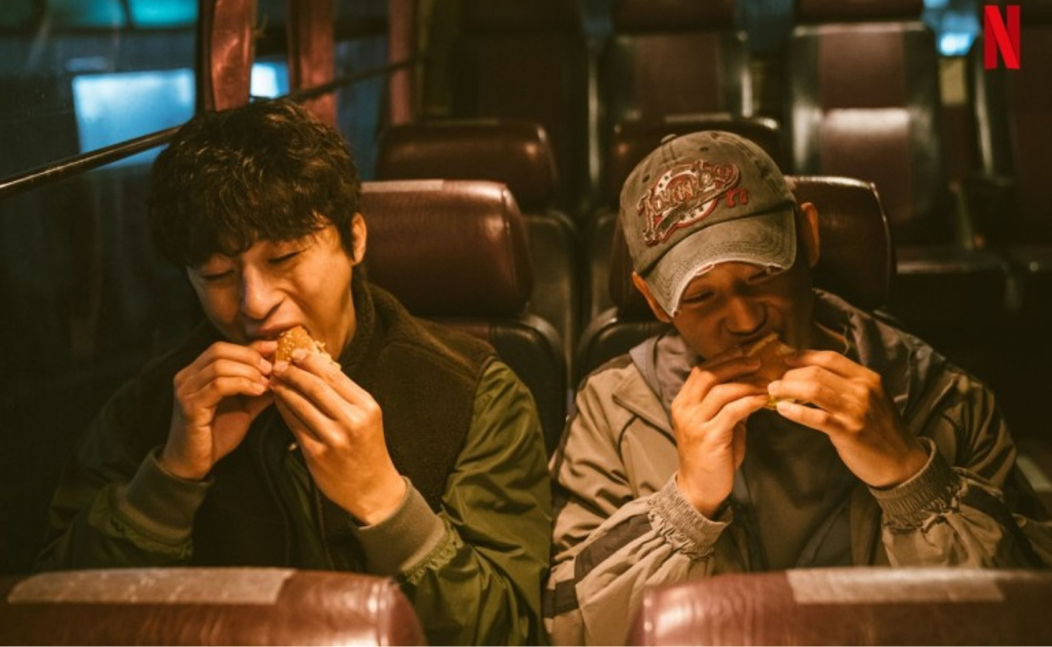넷플릭스 디피의 한 장면. 구교환과 정해인이 버스에 앉아 빵을 먹고 있다.