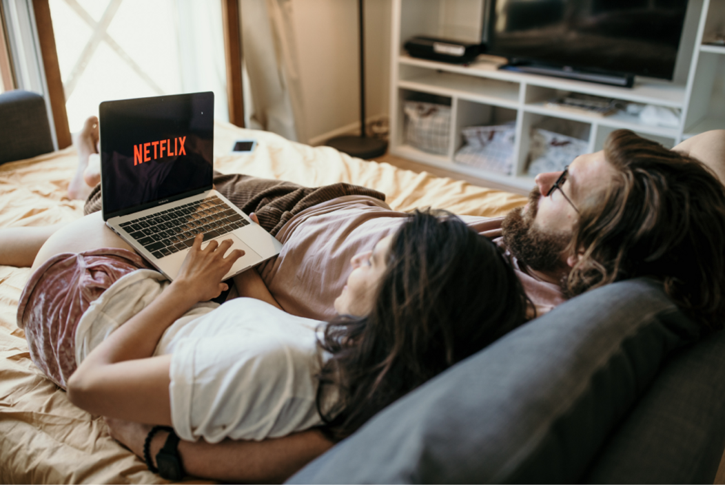 NETFLIX 화면이 적힌 노트북을 바라보며 침대에 누워 있는 두 남녀.