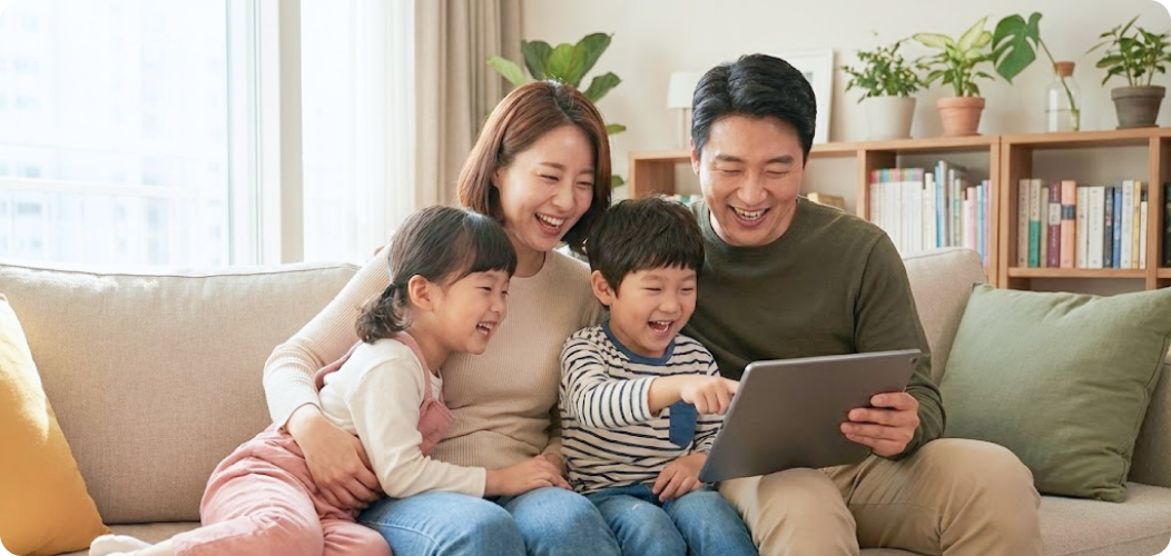 거실 소파에서 가족 네 명이 함께 태블릿을 보며 즐겁게 웃고 있는 모습의 따뜻한 분위기 이미지